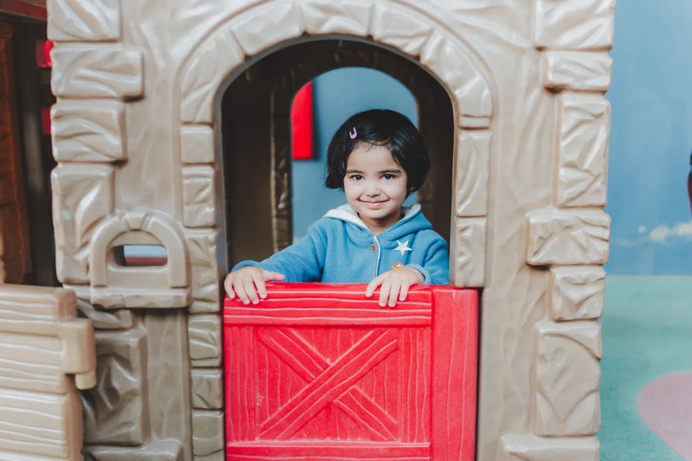 A smiling girl playing inside the toy playhouse