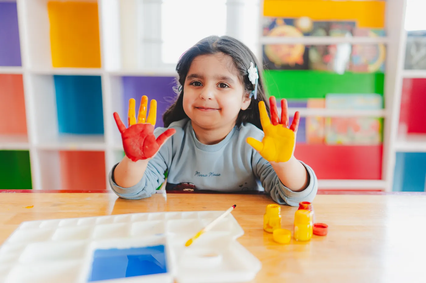 A smiling girl showing off her red and yellow painted hands