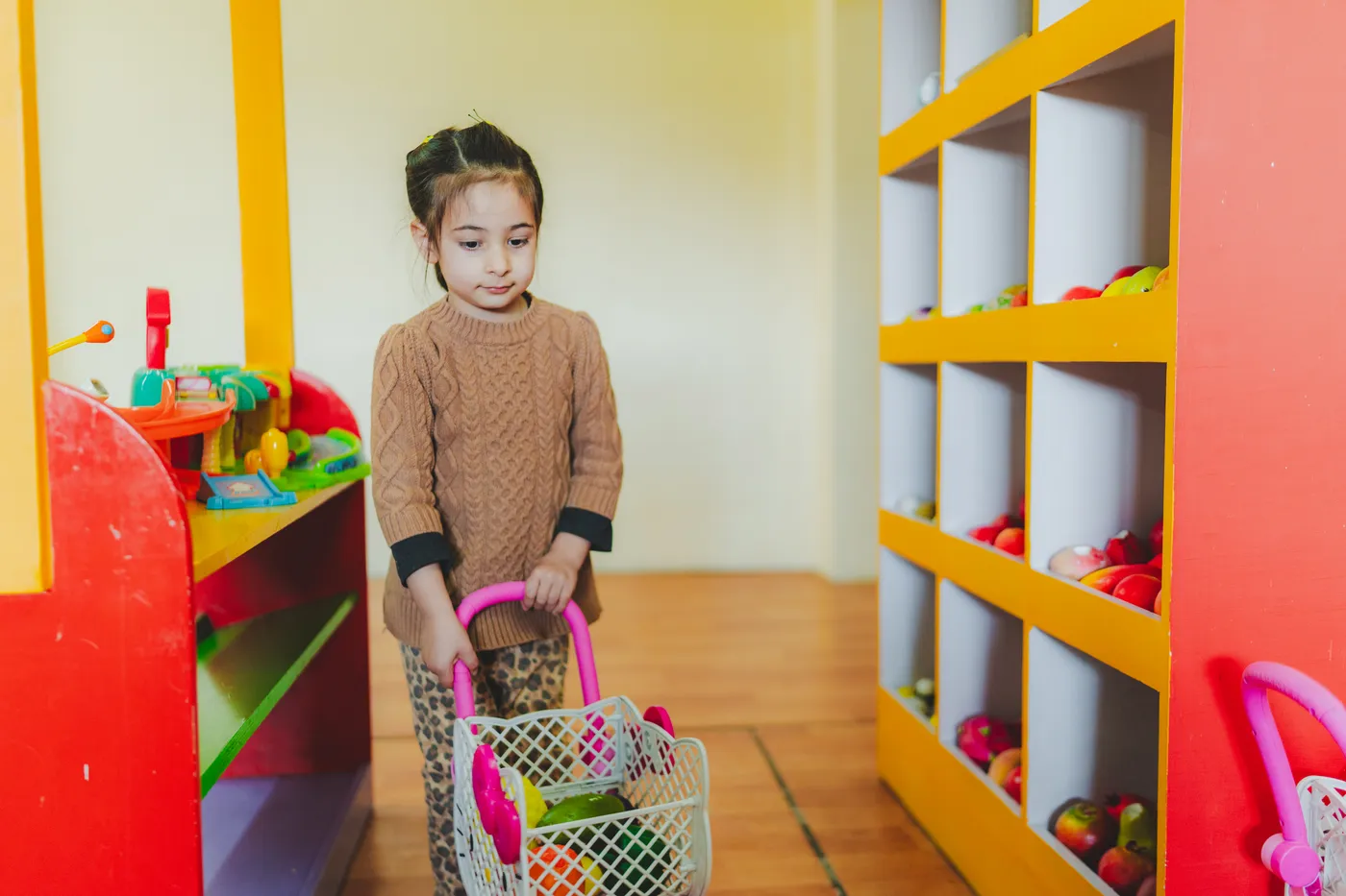 A girl with a shopping basket at the pretend grocery shop
