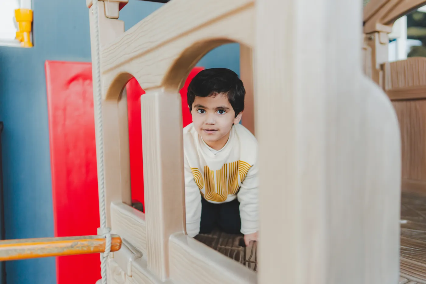 A boy peeking out from the wooden climbing frame